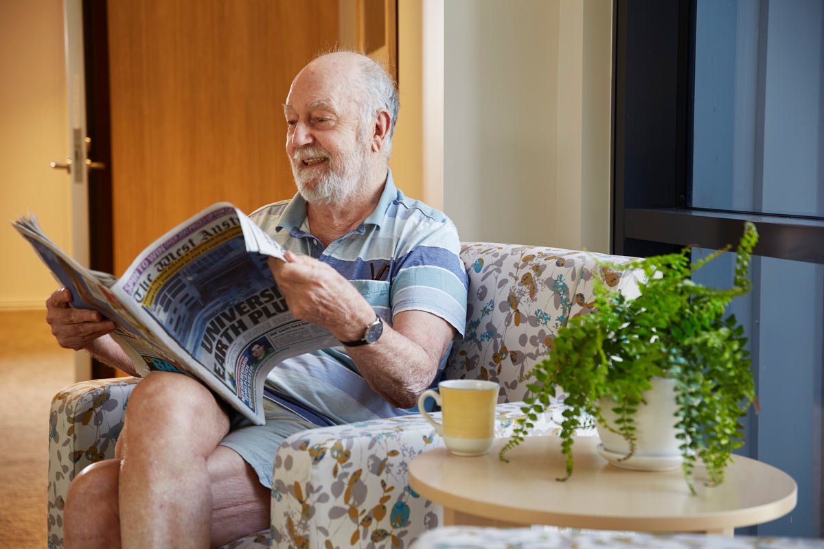 St Vincent's Aged Care resident reading a newspaper on a couch