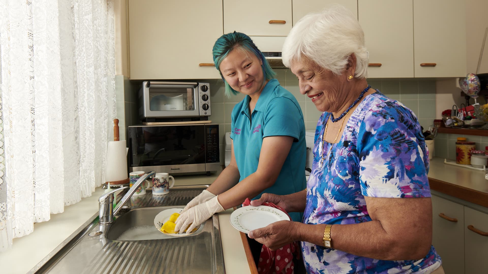 Home care support worker assisting elderly woman with the dishes