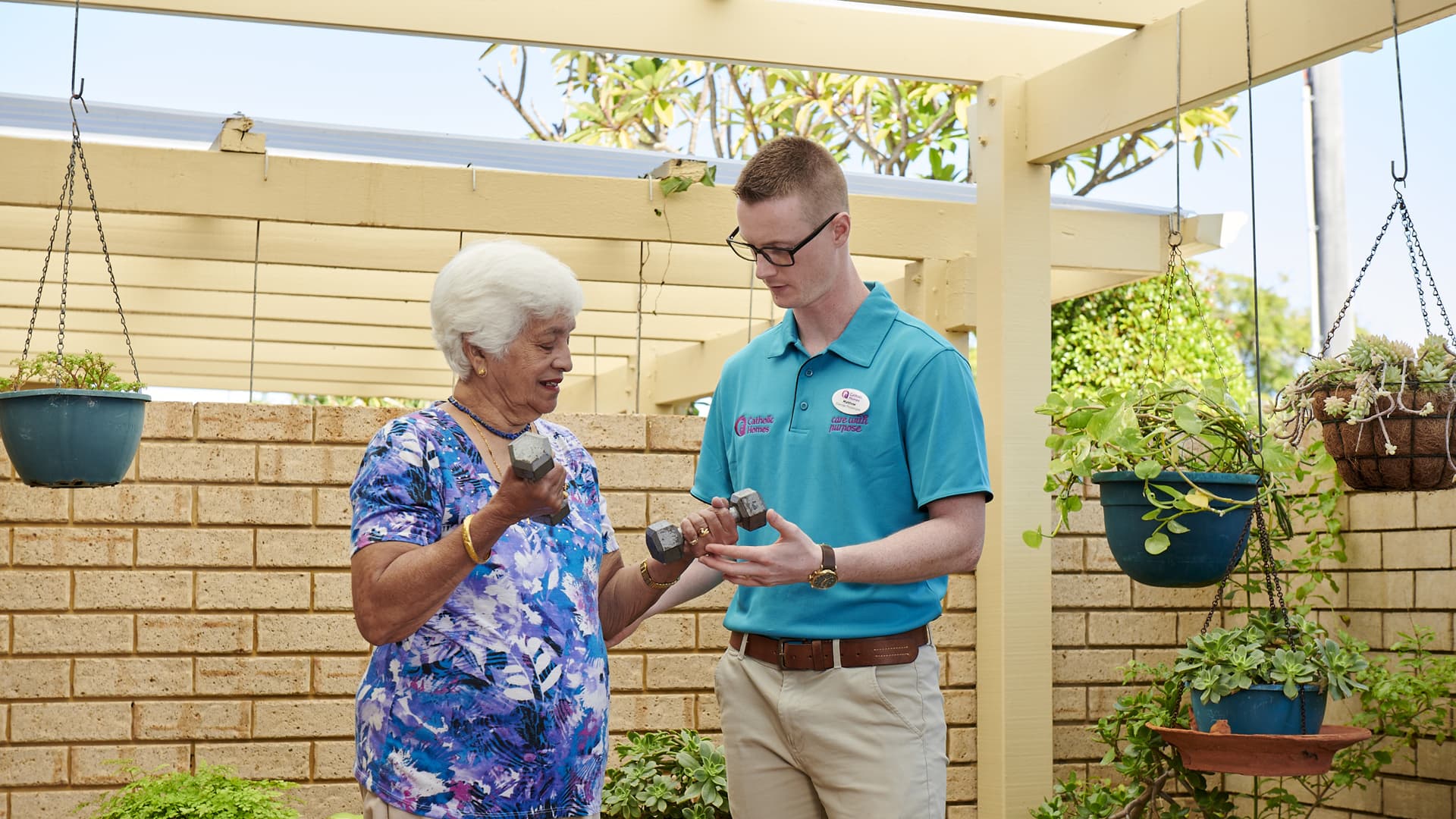A physio helping elderly lady with hand weights