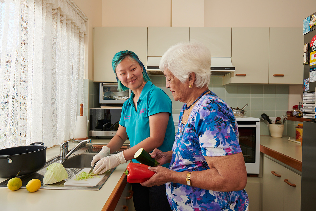 Lady helping elderly person with preparing food.